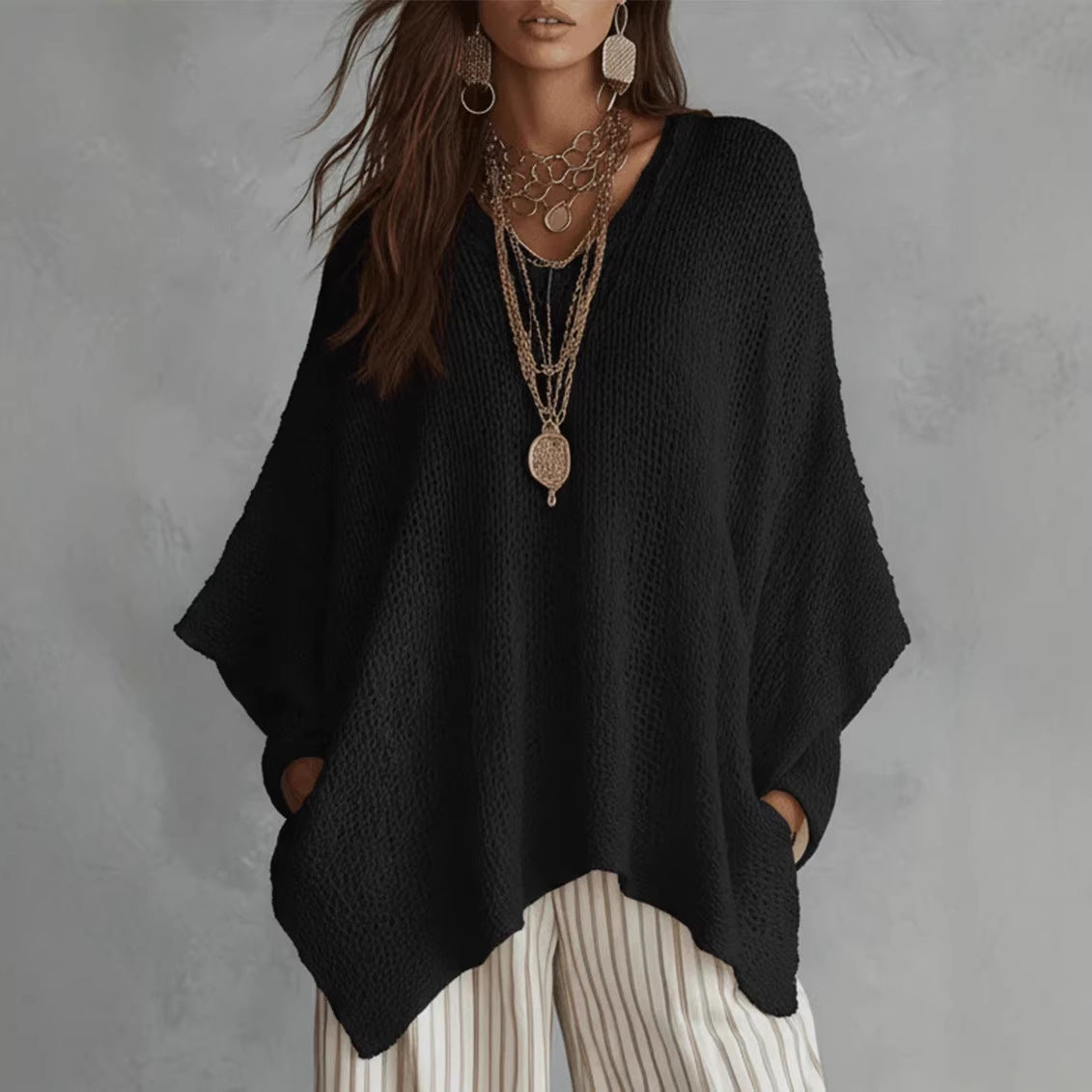 Oversized open-knit top in black, front view on model, V-neck, dolman sleeves, asymmetric hem, paired with striped pants