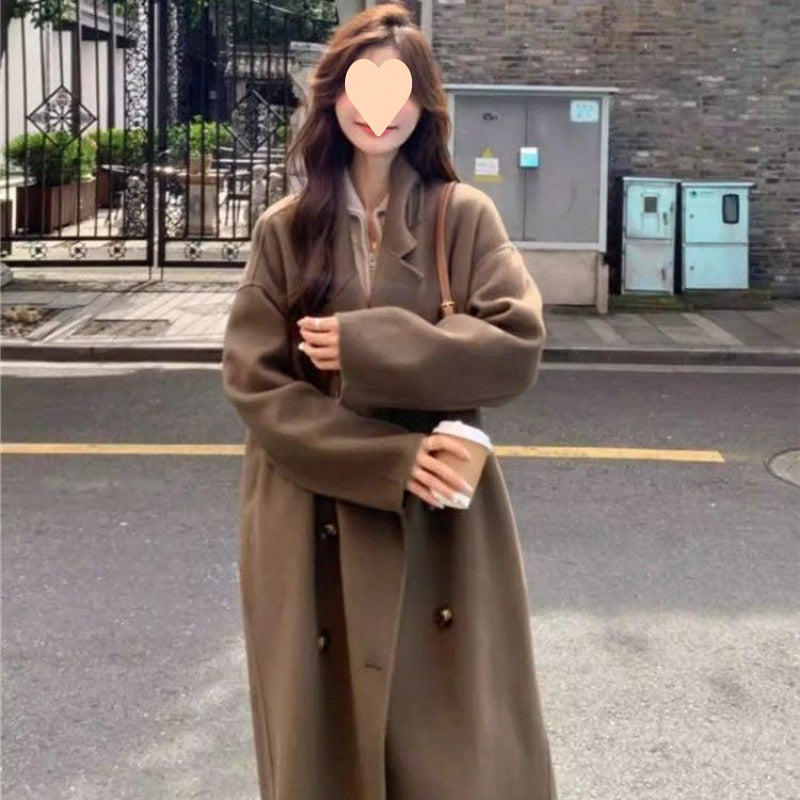 Long oversized double-breasted coat in caramel mocha, worn by a model on a street, front view with hands crossed