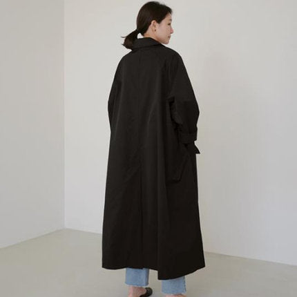 Black long button-front trench coat with flap pockets, back view on model, plain white background