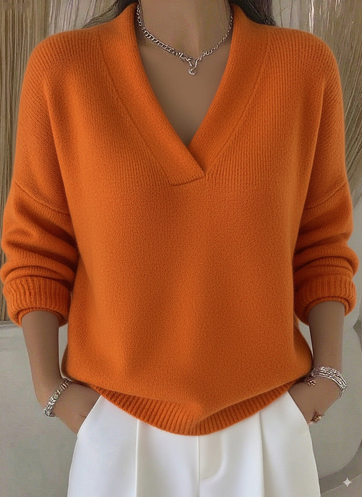 Orange relaxed V-neck knit sweater worn by a model with hands in white trousers pockets, front view