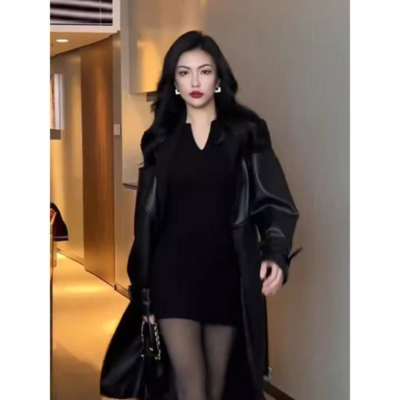 Front view of long black trench coat with contrast shoulders, worn by a model in a modern indoor space