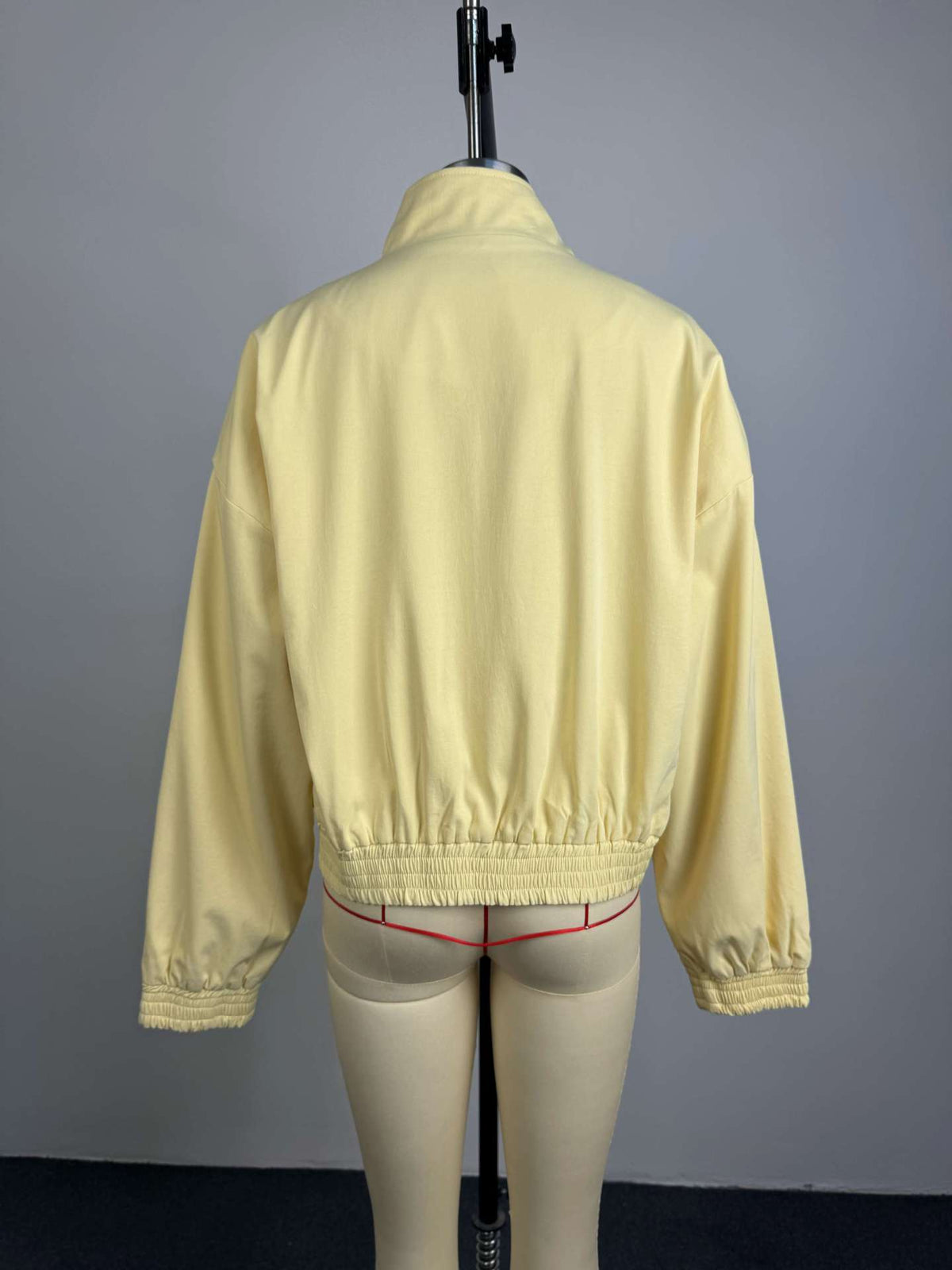 Pale yellow cropped bomber jacket, back view on mannequin, plain back, stand collar, elasticated hem