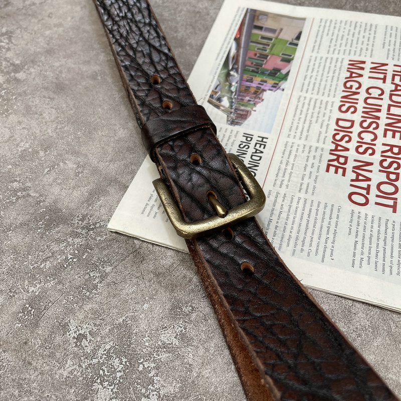 Leather belt dark brown, textured surface, bronze-tone buckle, on newspaper