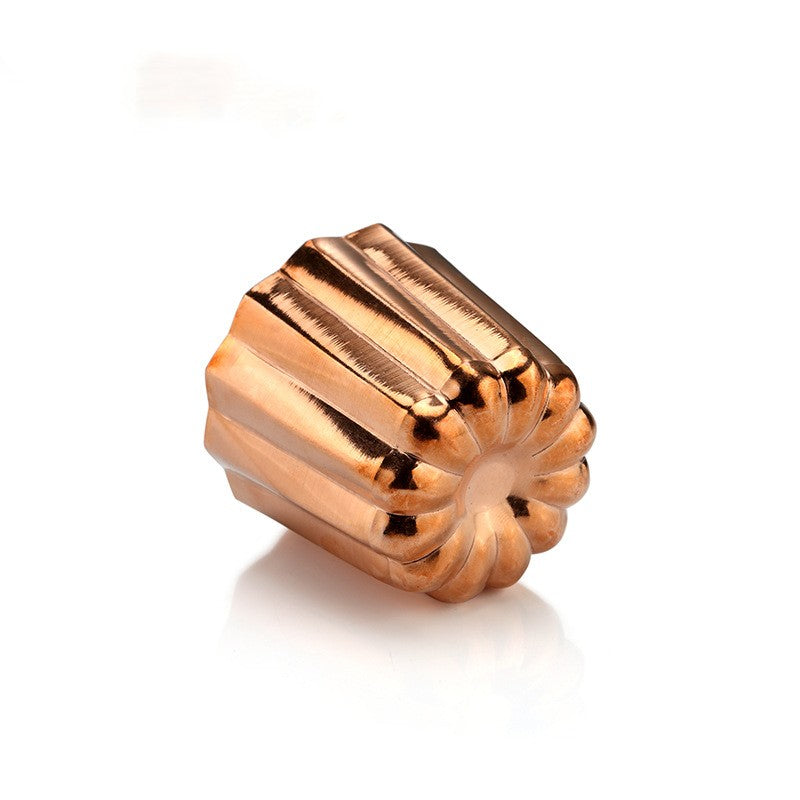 Copper canelé mould angled to show the fluted exterior and rounded base on a white background