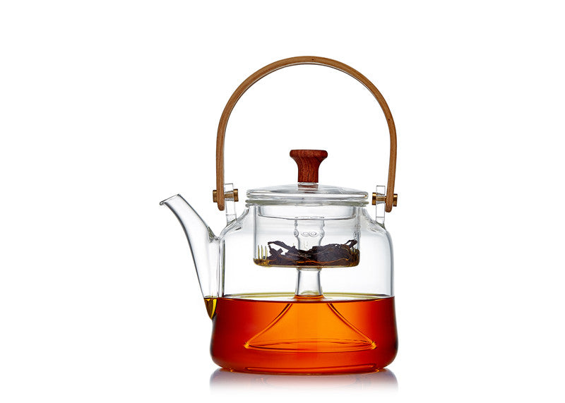Glass teapot with wooden handle and lid knob, front view, filled with tea and infuser, white background