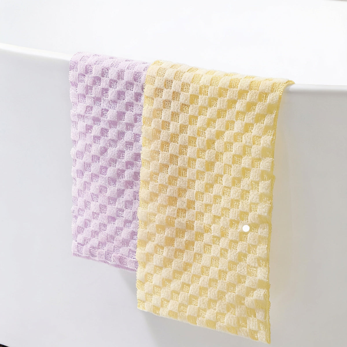 Two long nylon bath towels in lilac and yellow, draped over the edge of a white bath