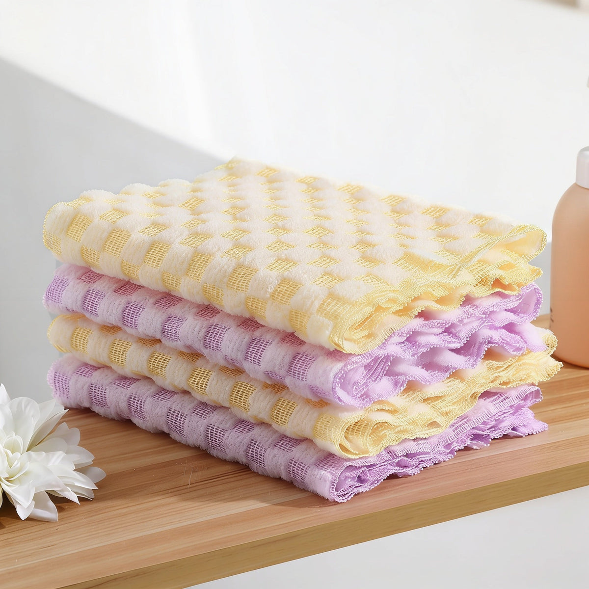 Stack of four folded long nylon bath towels alternating yellow and lilac, on a wooden shelf