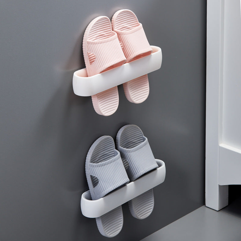 Wall-mount slipper rack in white, holding pink slippers, mounted on a grey wall, front view, in use