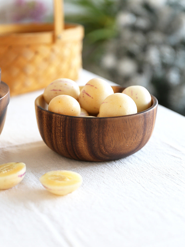 Wooden bowl with dark grain filled with small round fruits on a white table