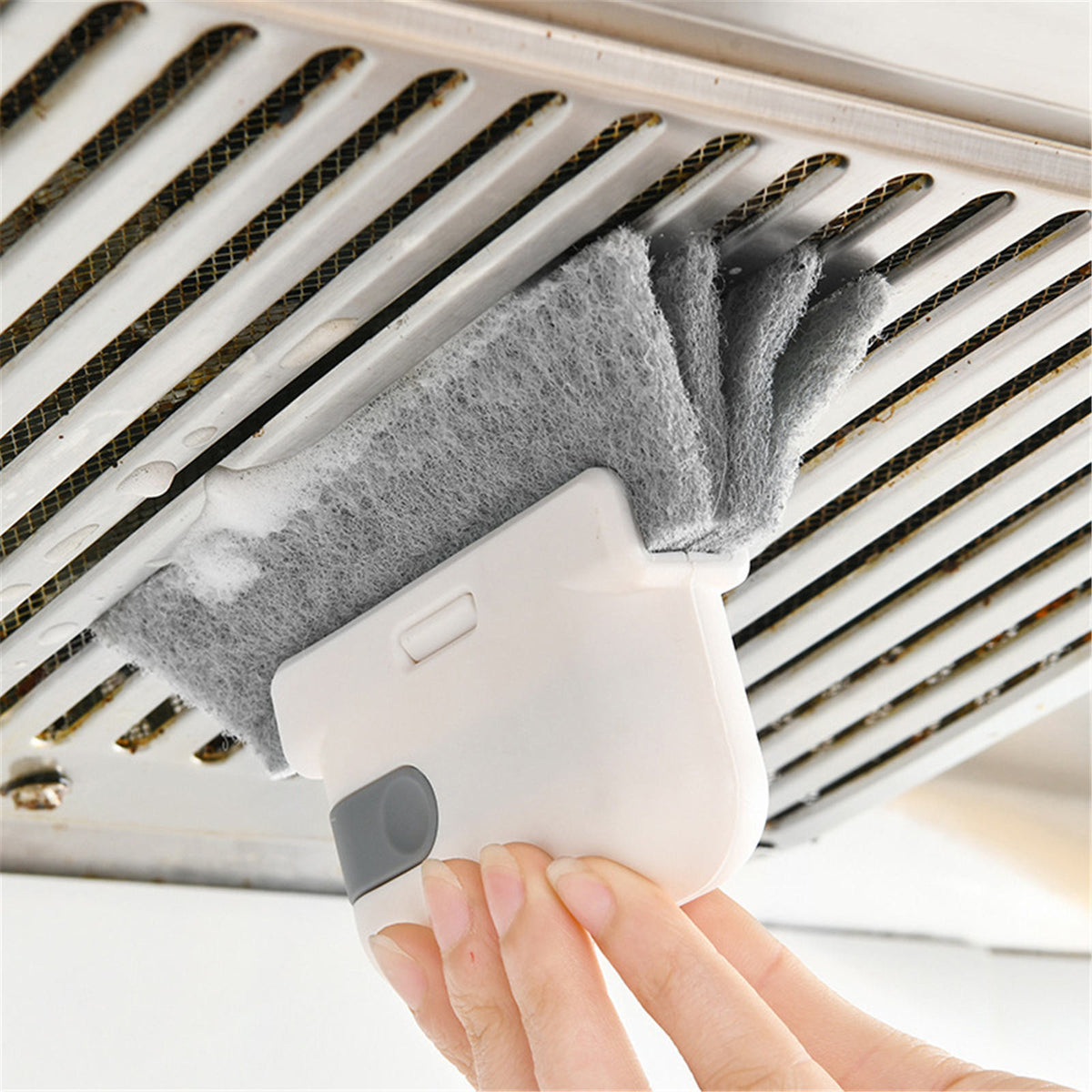 Cleaning brush with grey pad used to clean an air vent grille, held by hand