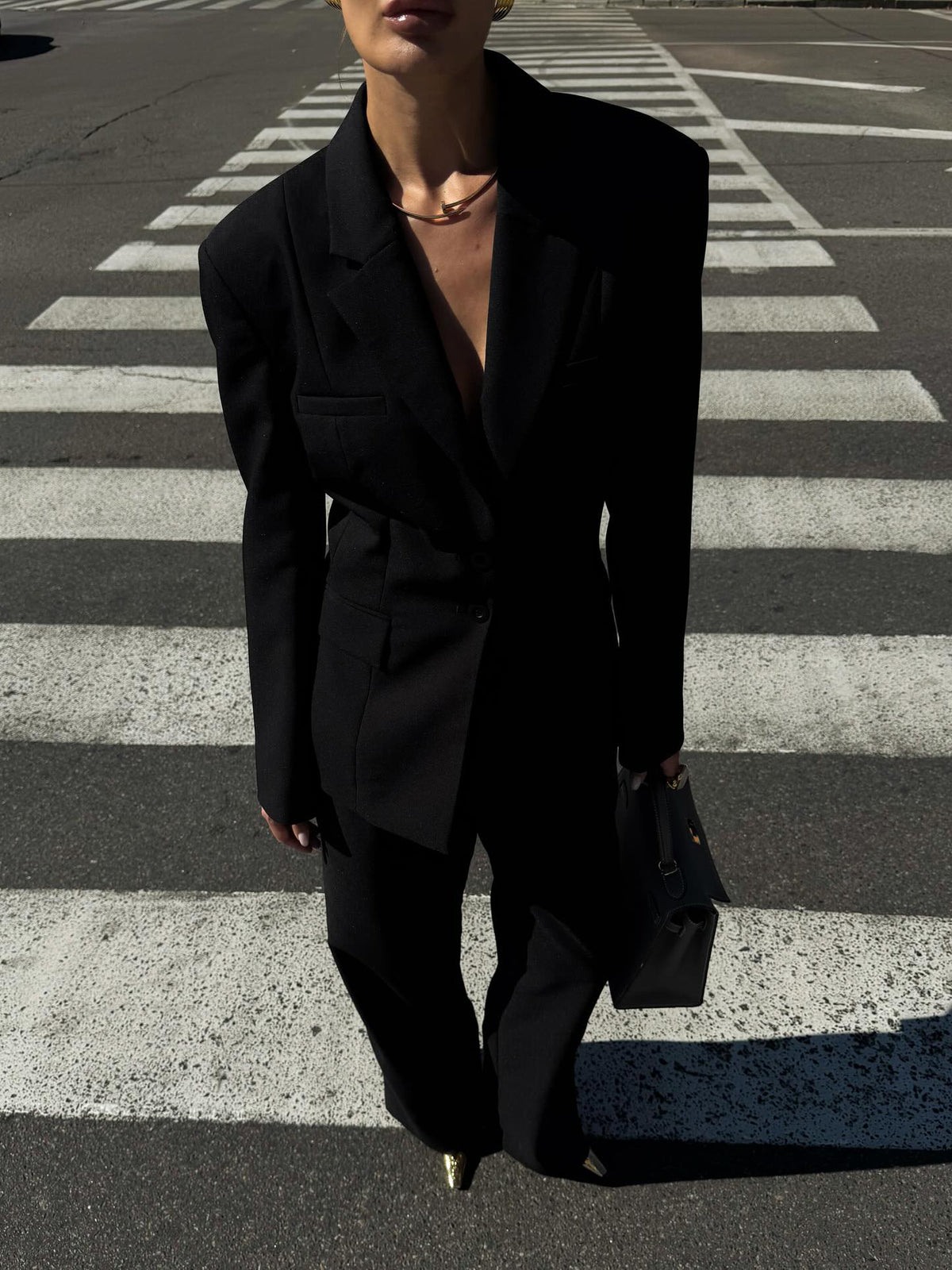 Front view of the black open-back blazer and wide-leg trouser suit on a model standing on a zebra crossing