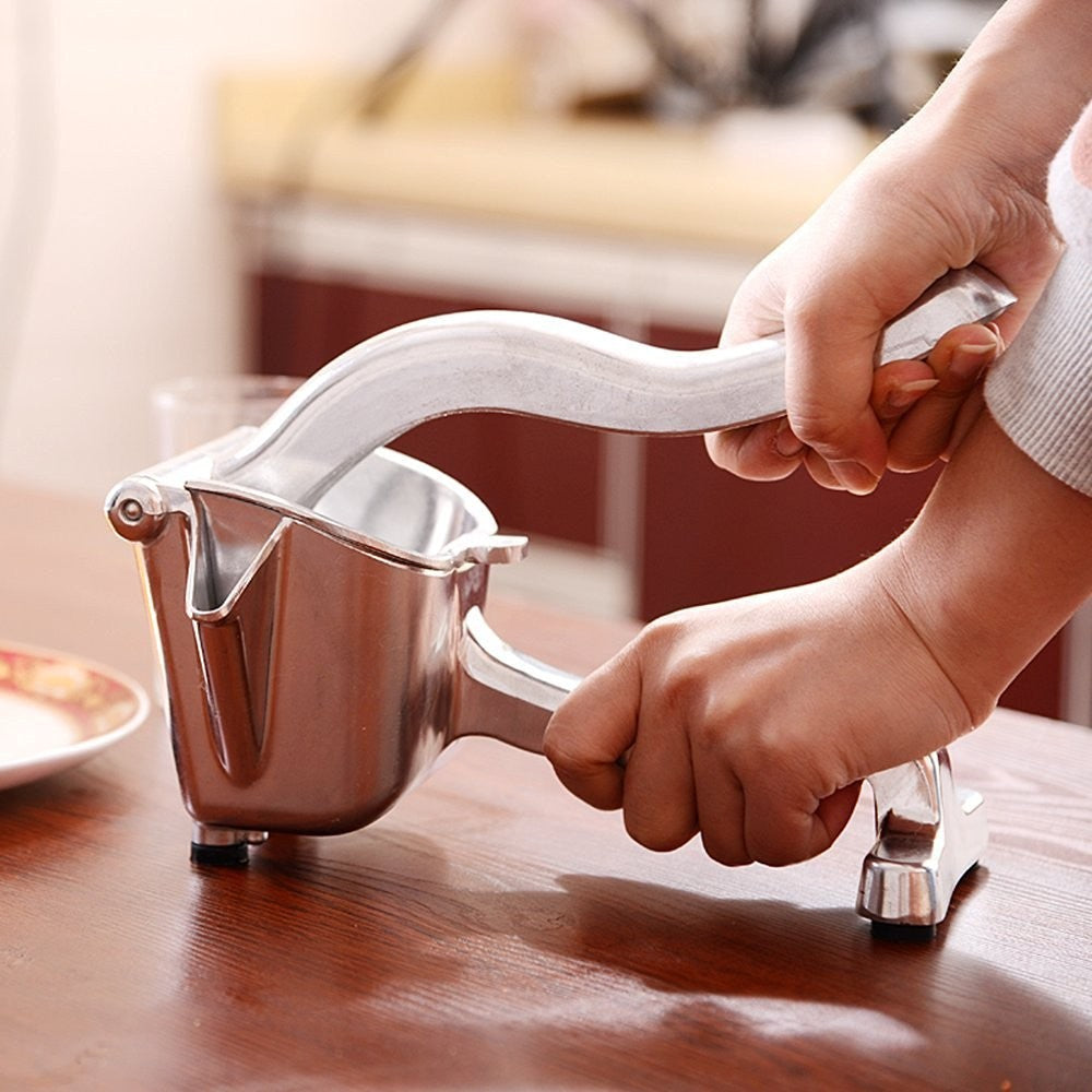 Aluminium hand-lever citrus press in use, hands pressing lever on wooden table