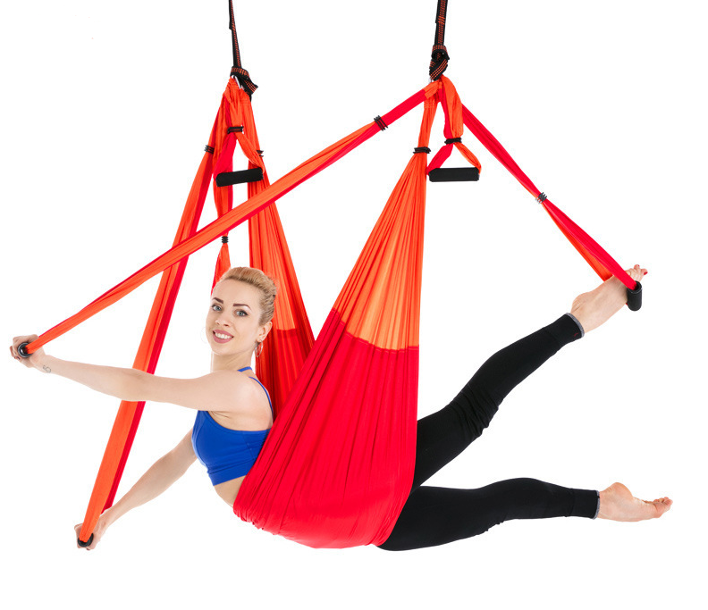 Red and orange two-tone aerial yoga hammock with handles, model in a side reclined pose