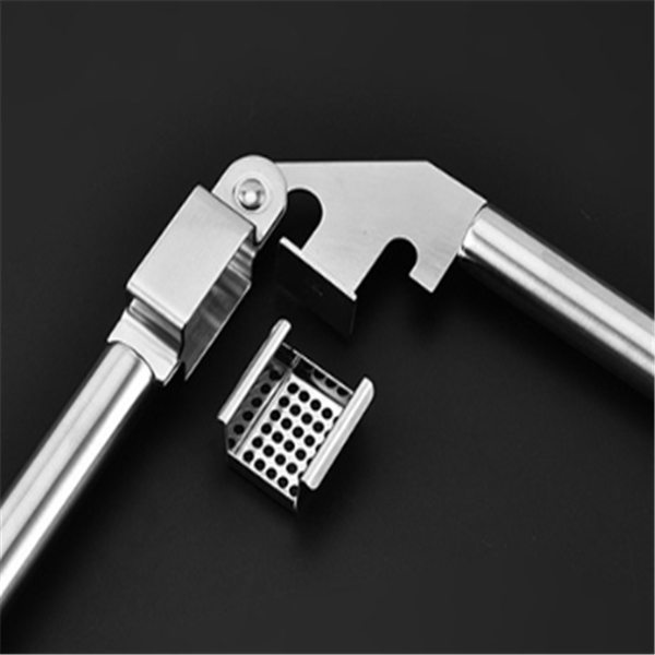 Detached perforated plate of stainless steel garlic press shown next to the main body on dark surface
