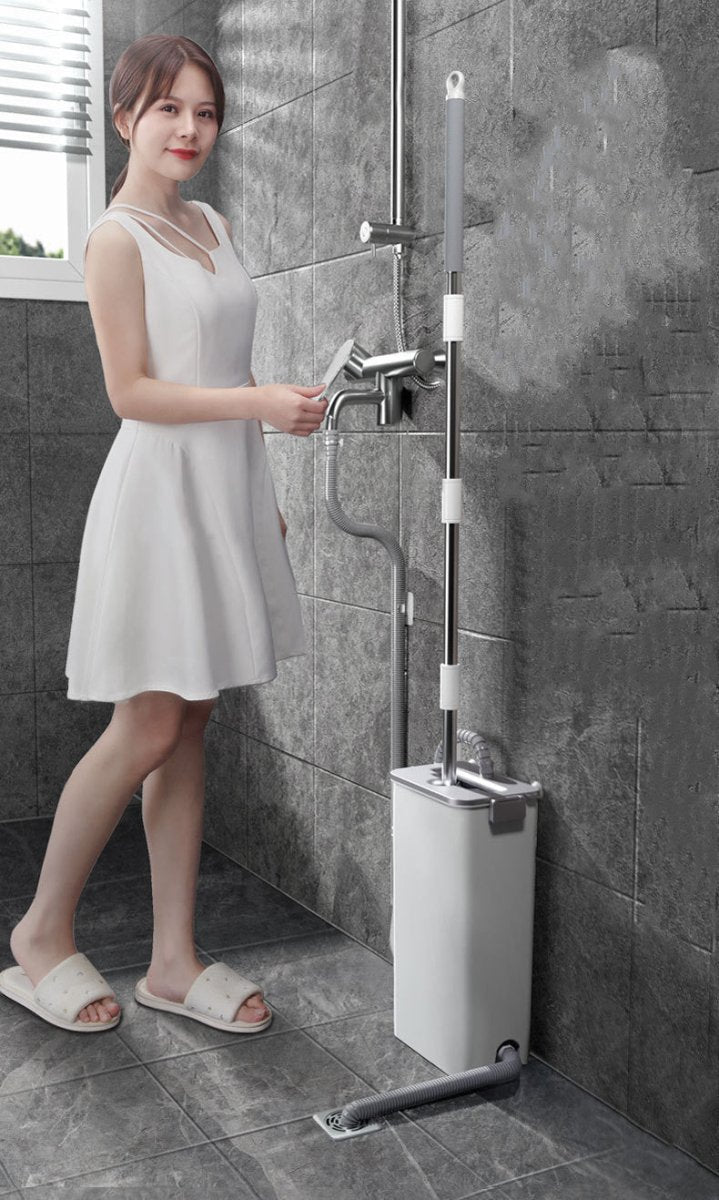 Woman in a white dress holding the mop handle next to the bucket set up by a shower tap