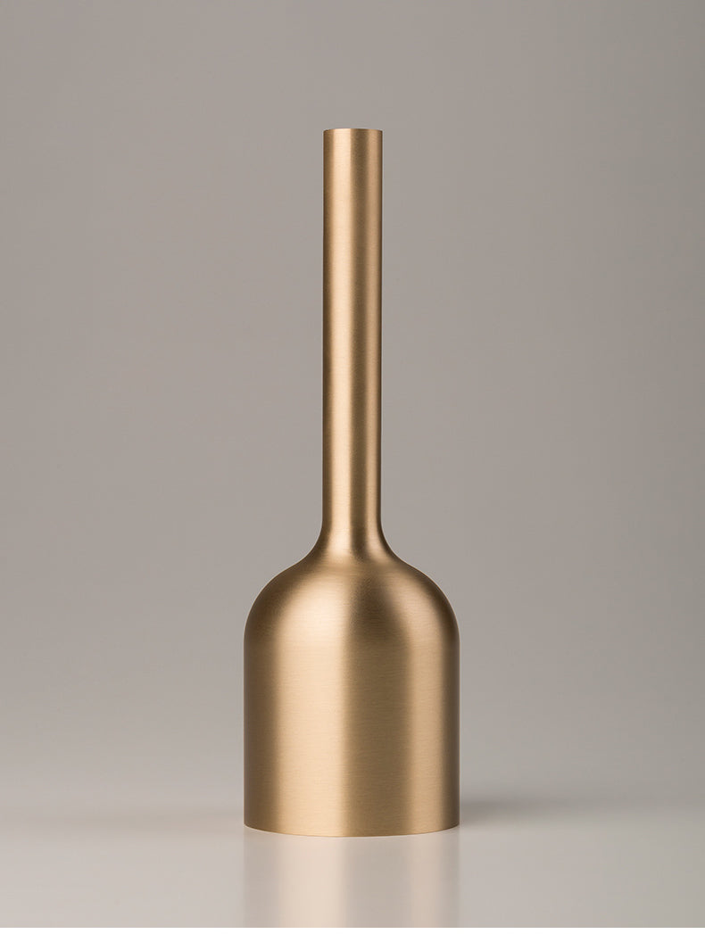 Brushed gold-tone metal bud vase with narrow neck on a neutral background