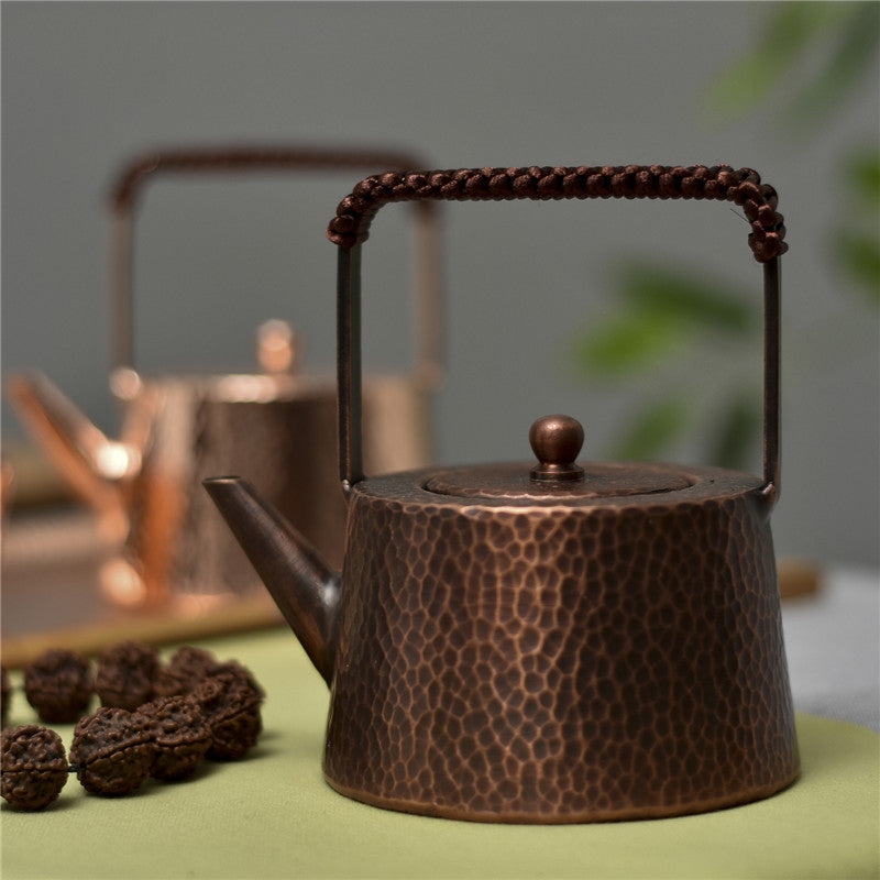 Hammered copper teapot with braided handle, side view on green cloth, dried fruits beside