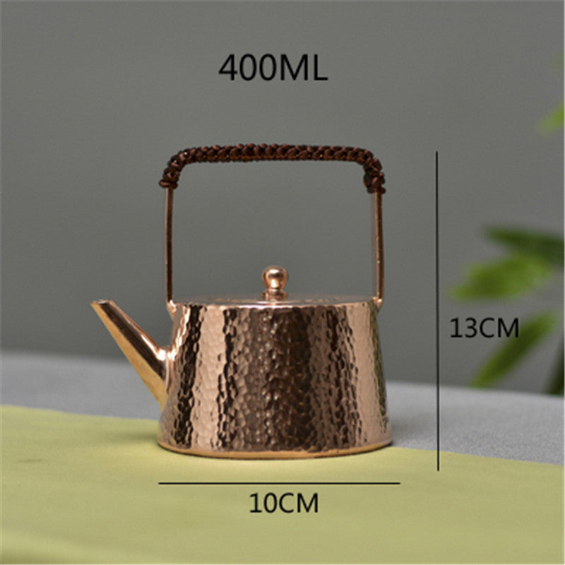 Hammered copper teapot with braided handle, front view on green cloth, size labels visible