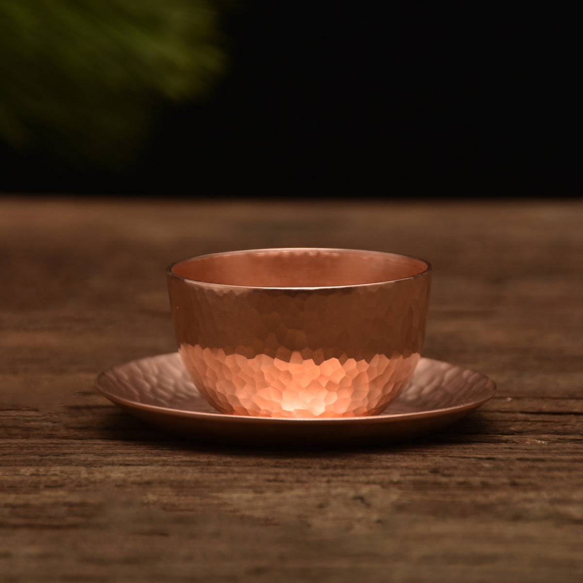 Hammered copper-tone teacup with saucer, bottom half textured, on wooden surface
