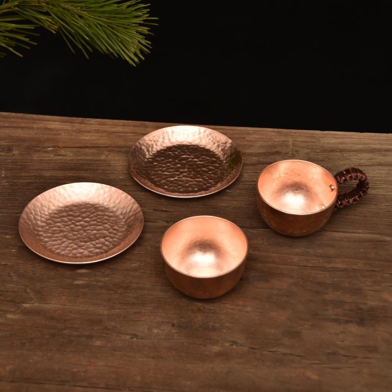 Hammered copper-tone cup, saucer, and two plates arranged on wooden surface