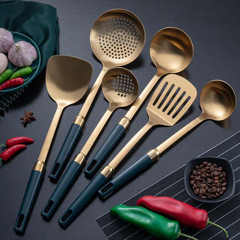 Gold-tone stainless steel kitchen utensils with teal handles, flat lay on dark surface with vegetables and spices