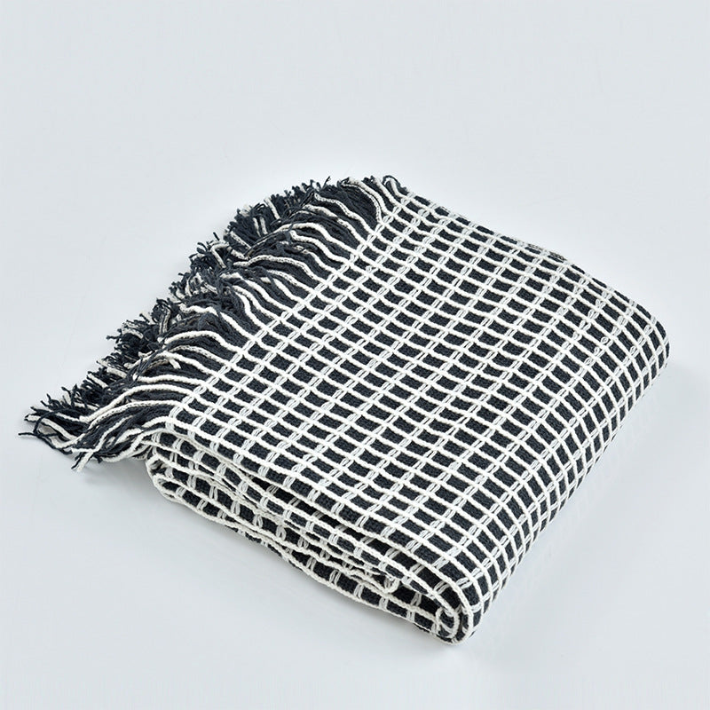 Folded waffle-weave throw blanket with tassel fringe on a plain white background