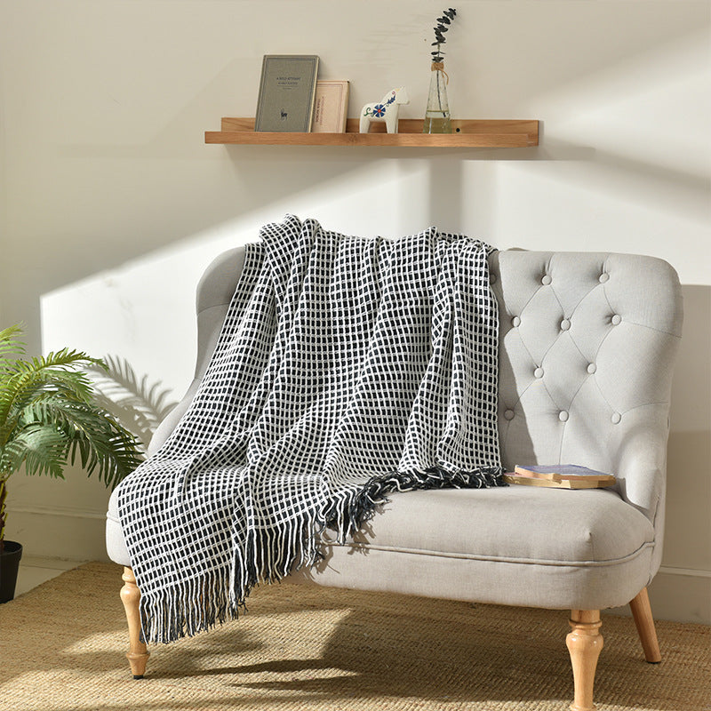 Waffle-weave throw blanket with tassel fringe laid over a light grey tufted armchair