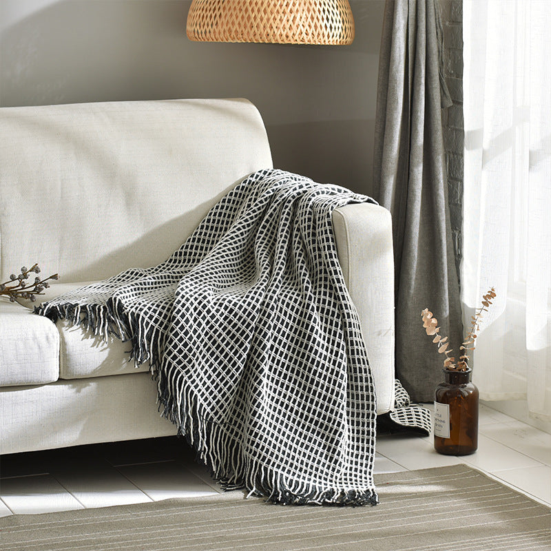 Black and white lattice throw blanket with tassel fringe draped over the arm of a white sofa