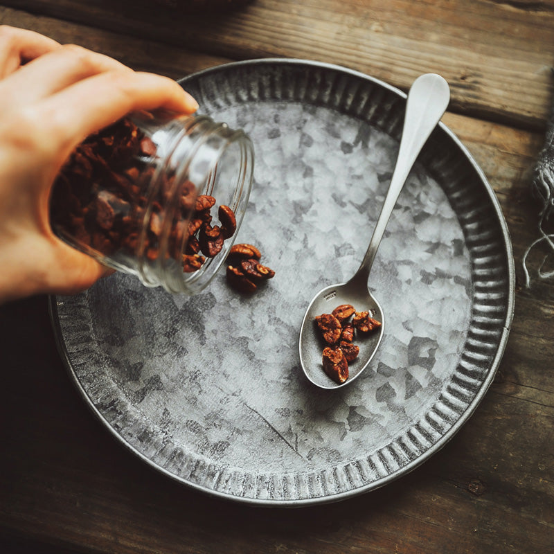 Ribbed iron serving tray with weathered finish, flat lay on wooden surface, spoon and jar of nuts being poured