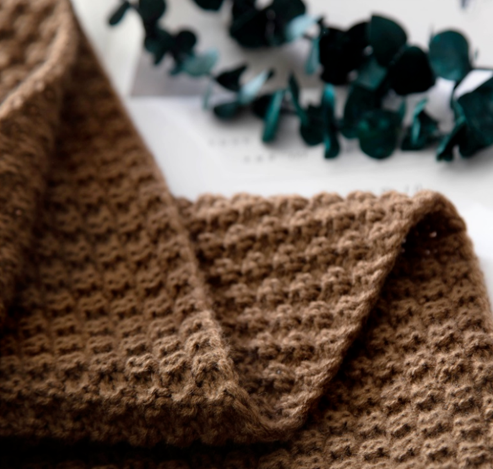Close-up of brown chunky knit throw showing textured pattern and soft fabric surface
