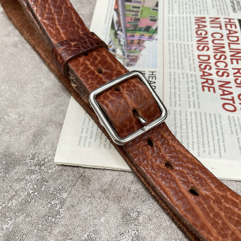 Leather belt tan colour, silver-tone buckle, textured surface, on newspaper