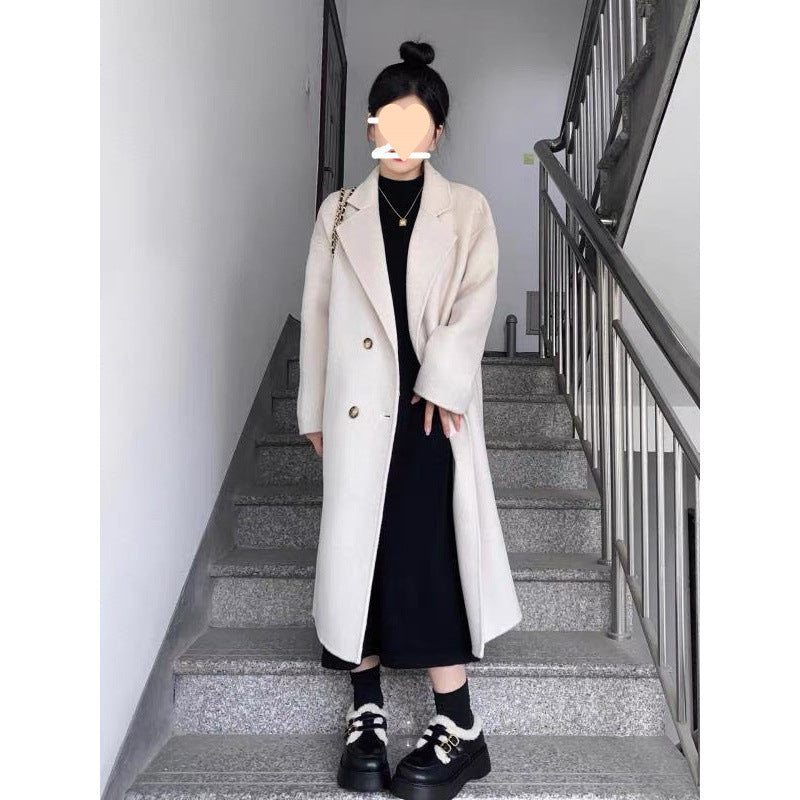 Long oversized double-breasted coat in oat white, worn by a model on stairs, front view with black outfit
