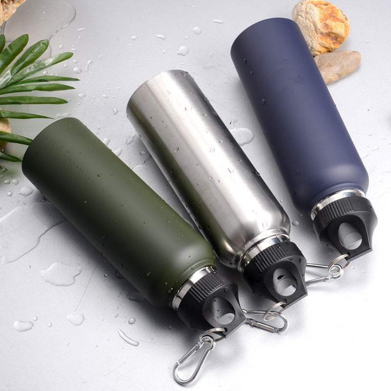Three stainless steel vacuum bottles in olive green, silver, and navy blue, lying flat on wet surface with water droplets