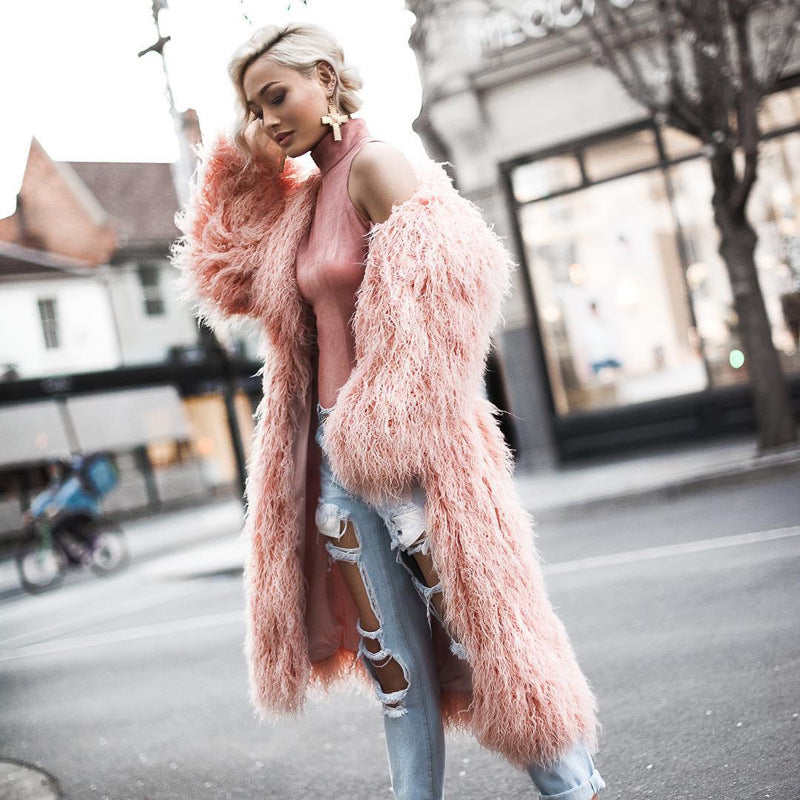 Shaggy faux-fur long coat in pink, worn open front on a model with ripped jeans, standing on a street.