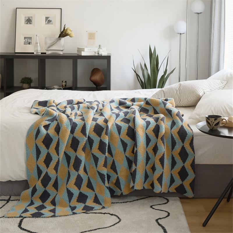 Geometric diamond-pattern knit throw in blue, mustard and charcoal, folded at foot of bed in modern bedroom setting