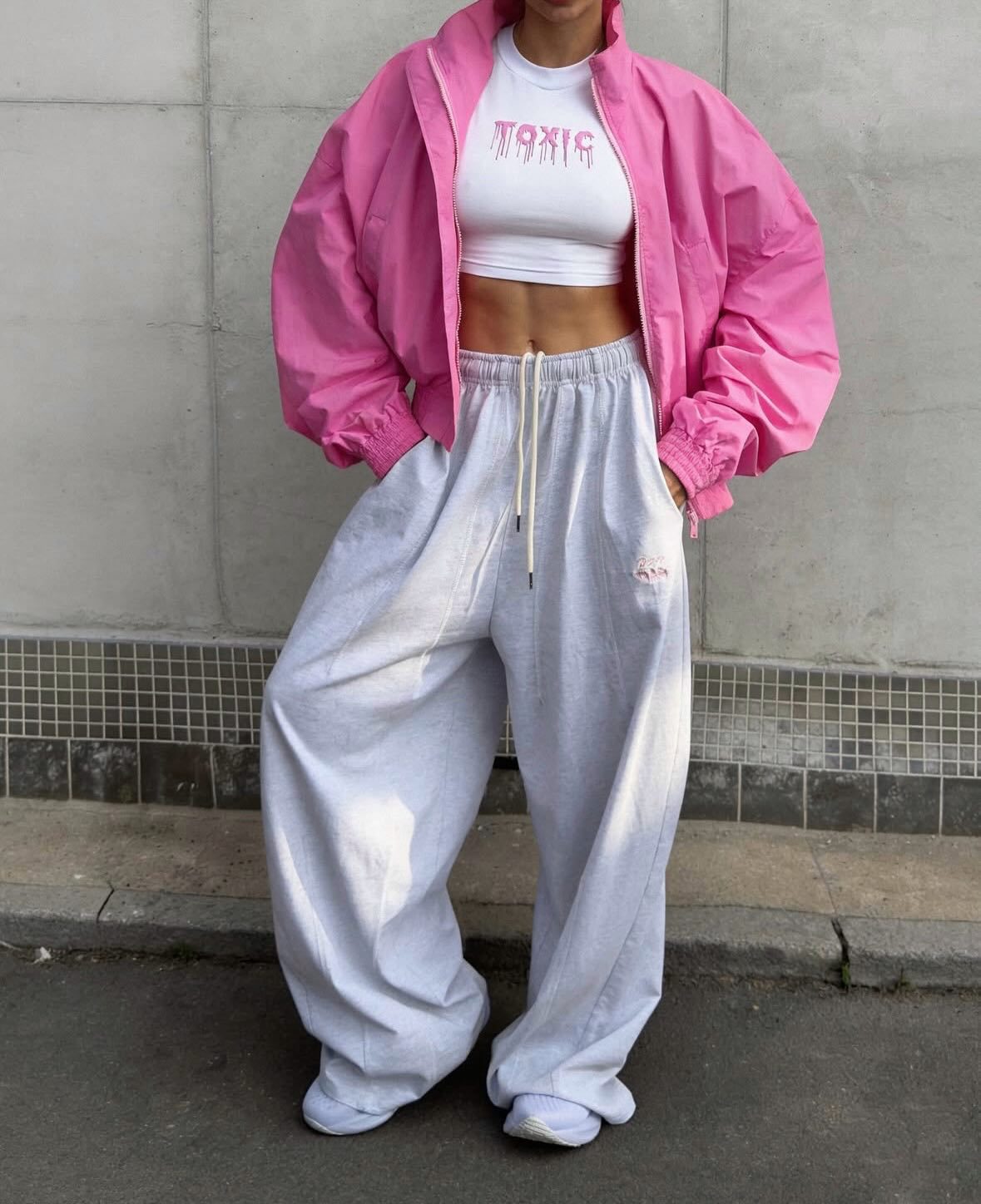 Bright pink cropped bomber jacket, front view on model, open, over white crop top and light grey wide sweatpants