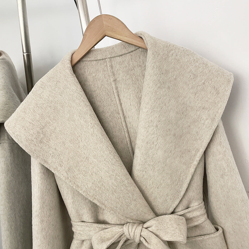 Close-up of beige short wrap coat with wide collar and tie belt, front view on hanger