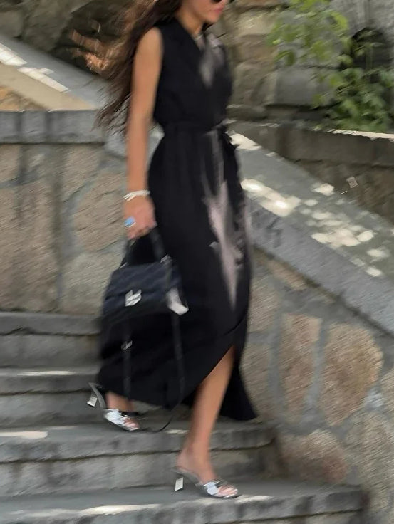 Sleeveless wrap blazer dress in black, side view on model walking up stone steps, carrying a bag