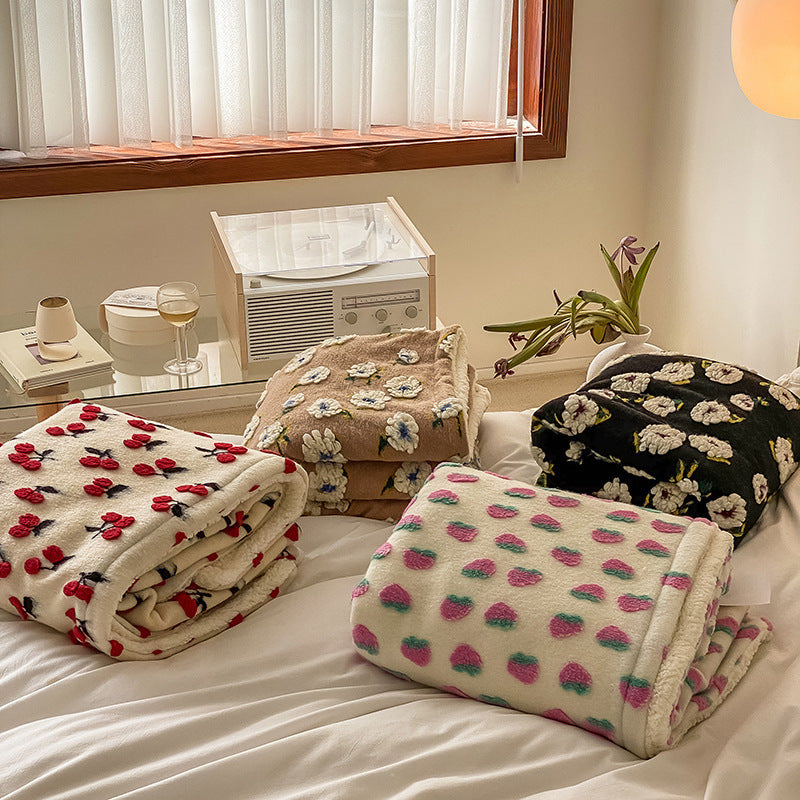 Double-Layer Tufted Flower Blanket in various patterns including cherries, strawberries, and flowers, folded on a bed with a