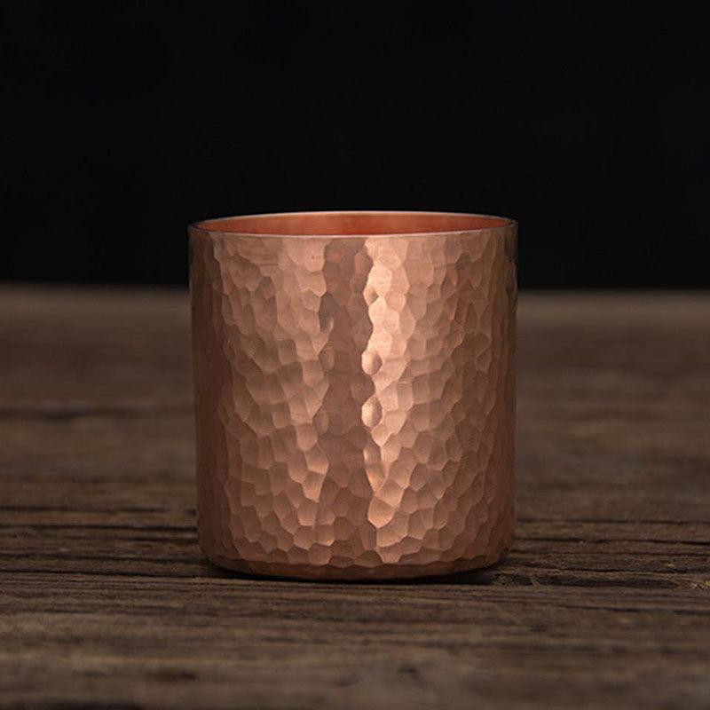Single hammered metal tea cup, copper colour, front view on wooden surface with dark background
