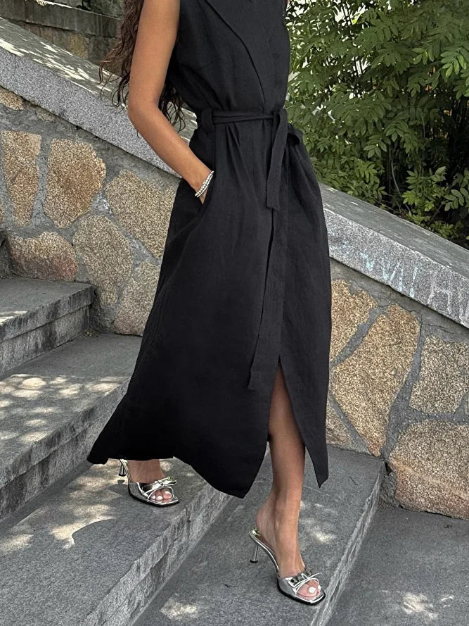 Sleeveless wrap blazer dress in black, side view of model on stone steps, highlighting the waist tie and slit
