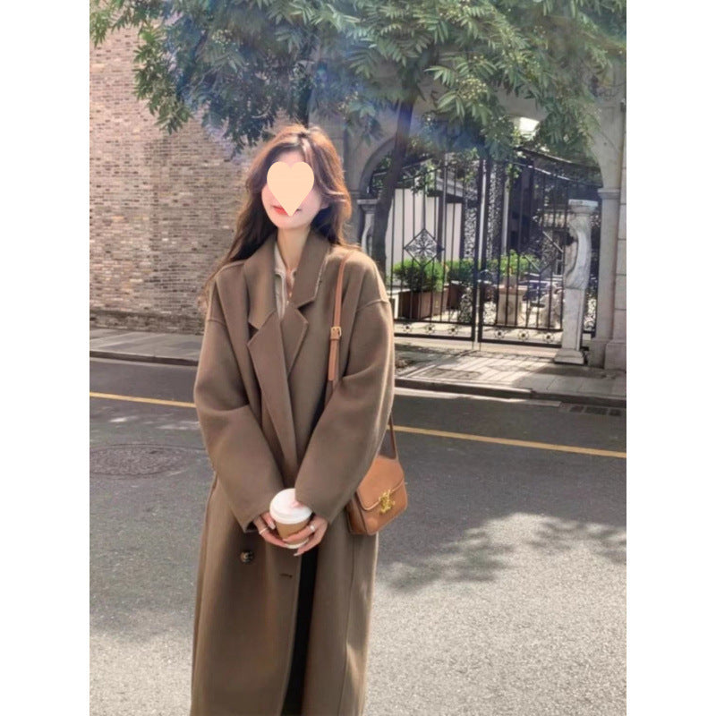 Long oversized double-breasted coat in caramel mocha, worn by a model on a street, front view holding a cup