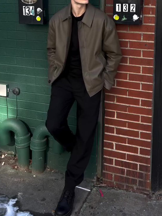 Olive leather-look bomber jacket worn open, model leaning against a brick wall with hands in pockets