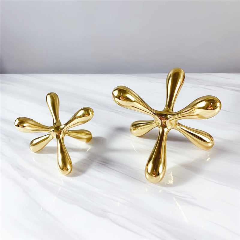 Two gold-tone metal jacks sculptures, different sizes, side by side on marble surface
