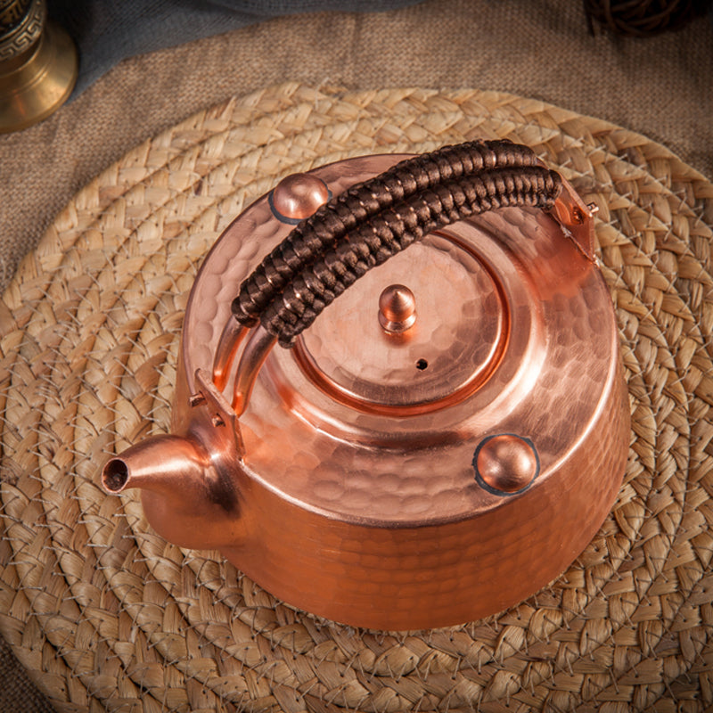 Overhead view of copper teapot with lid knob and vent hole, placed on a woven mat