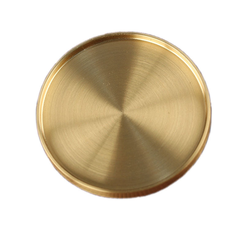 Top view of brushed gold-tone metal coaster, circular with radial texture on white background