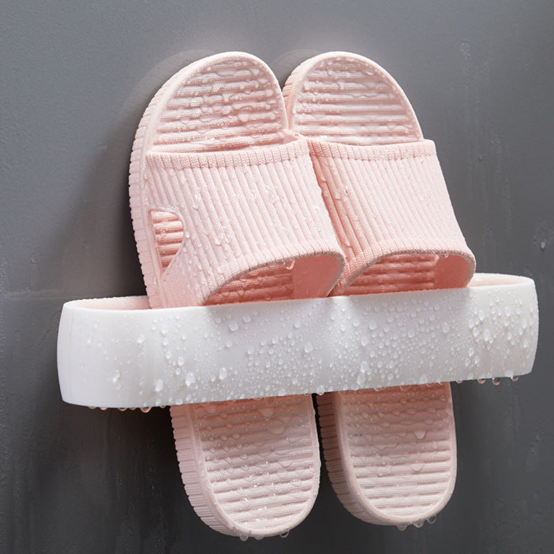 Close-up of white wall-mount slipper rack with pink slippers, water droplets visible, front view, in use