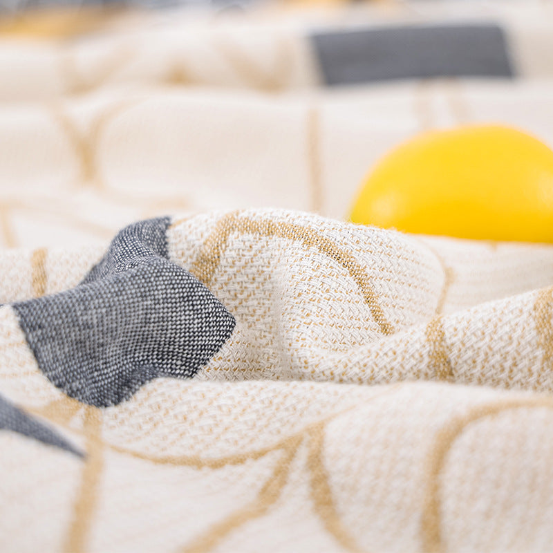 Close-up of the gauze weave of the card-suit blanket, showing cream base, gold-tone outline pattern and a solid grey spade shape