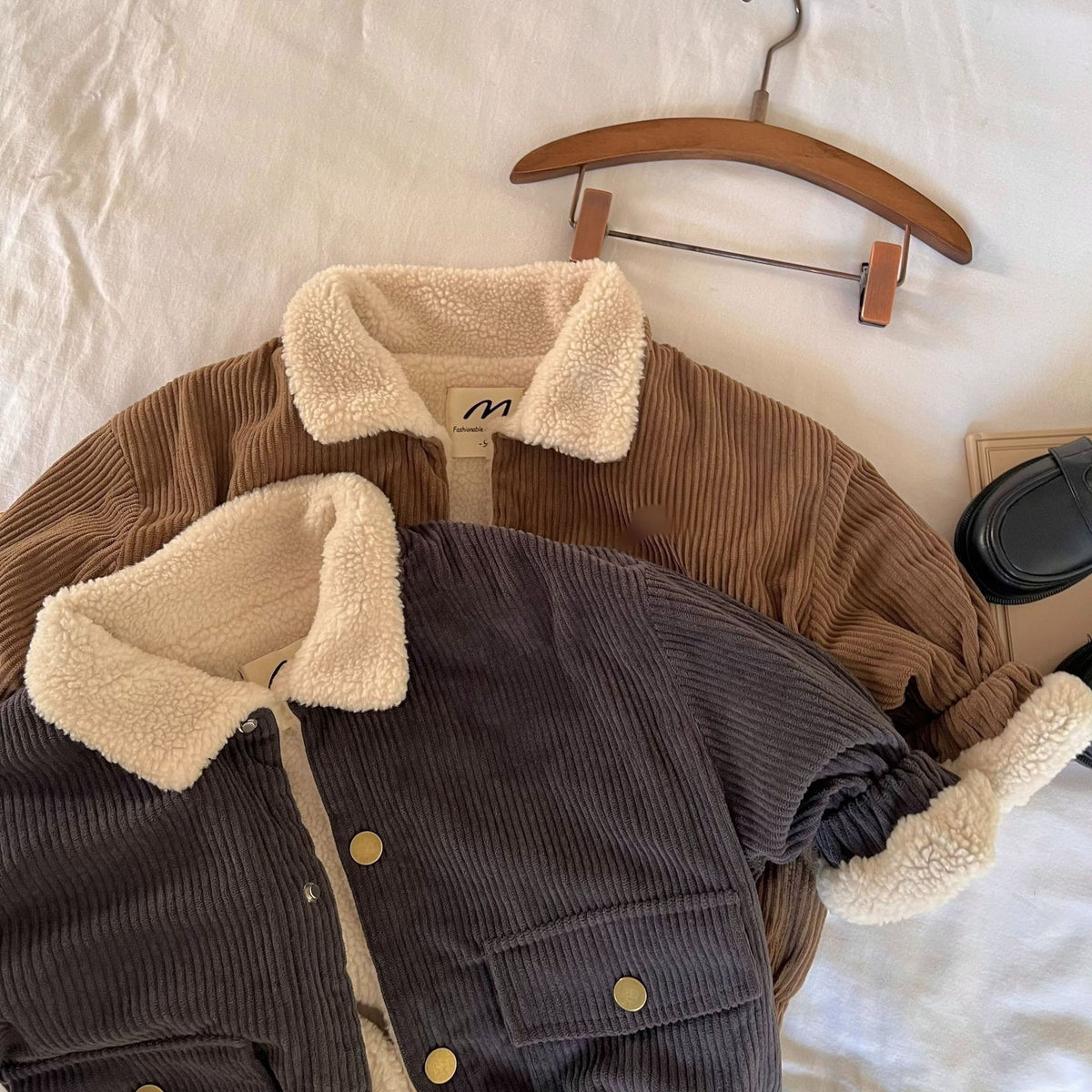 Dark grey jacket in front of the brown one, on a hanger