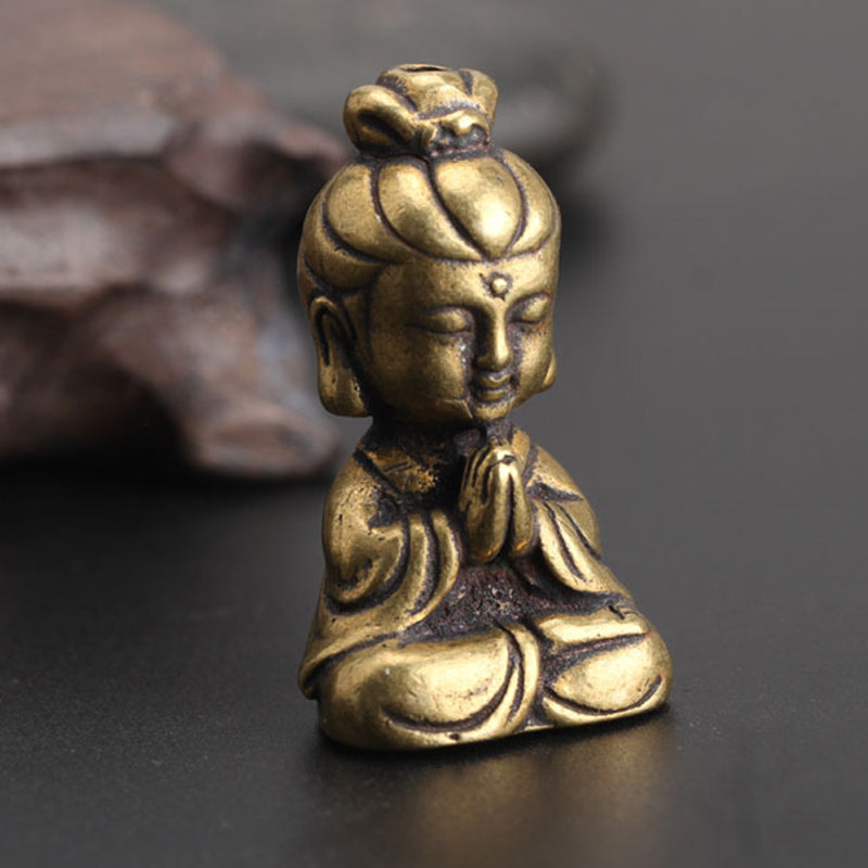 Small brass-look meditating figure ornament, three-quarter view, seated with praying hands and topknot, on dark surface